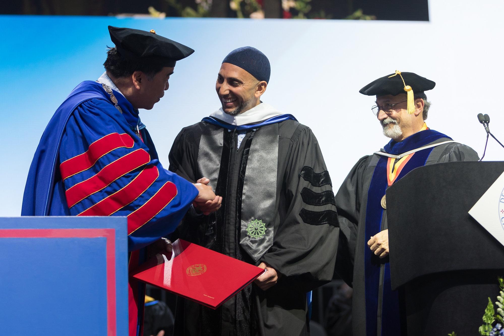 A. Gabriel Esteban, Ph.D., president of DePaul University, left, and Guillermo Vásquez de Velasco, dean, College of Liberal Arts and Social Sciences, right, congratulate honorary degree recipient Rami Nashashibi during the commencement ceremony at Wintrust Arena. Nashashibi, a 1996 alumna, is the founder and executive director of Inner-City Muslim Action Network. (DePaul University/Jeff Carrion)